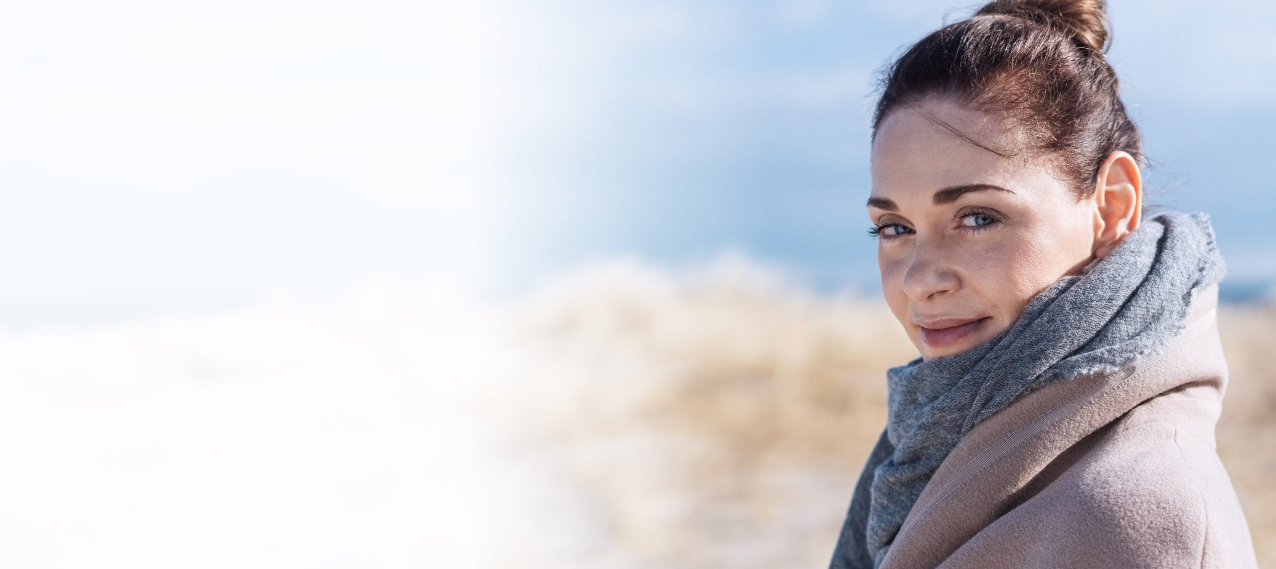 Junge Frau mit Schal bei sonnigem Wetter am Strand